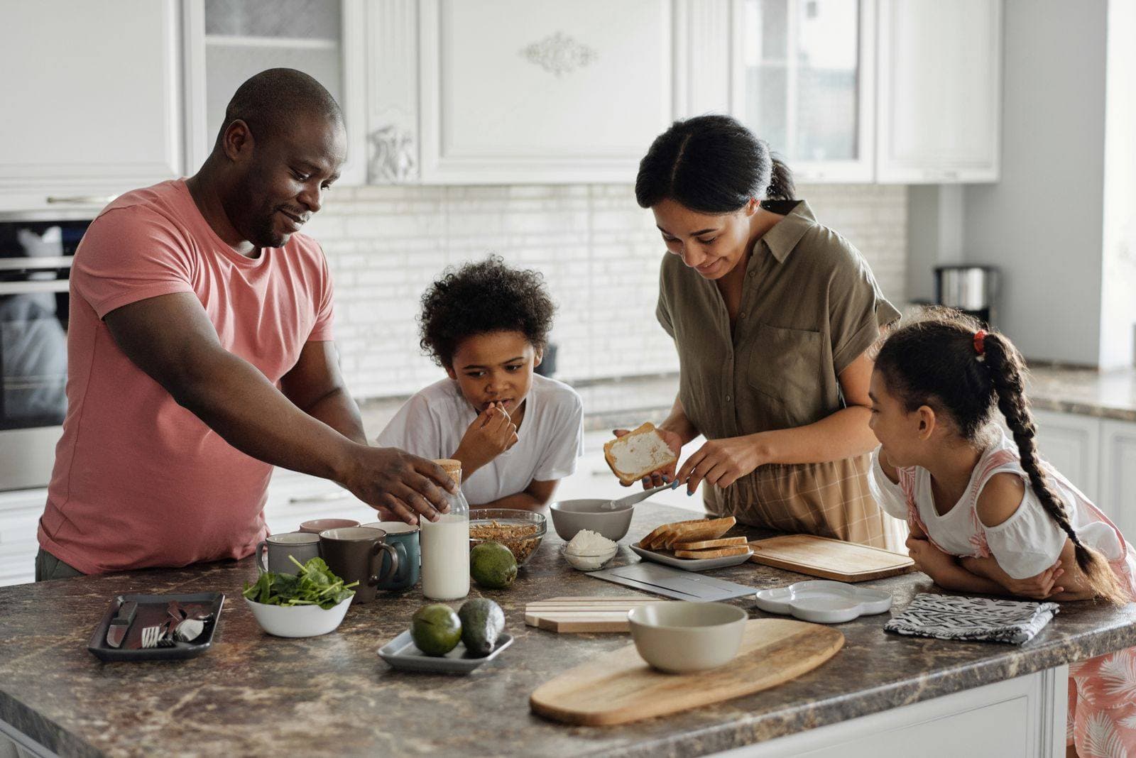A family of four making breakfast together around a kitchen island