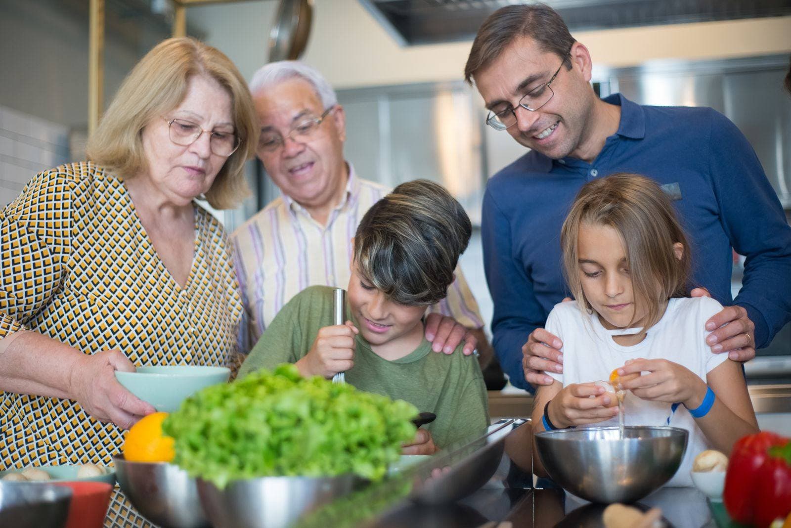 A multigenerational family cooking together — the kids crack eggs while dad keeps a hand on each shoulder